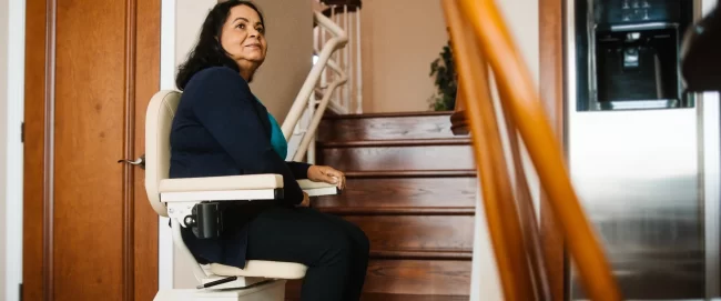 A woman sitting in a stairlift at the bottom of a staircase.