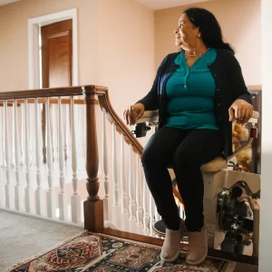 A woman sitting in a stairlift at the top of the stairs.