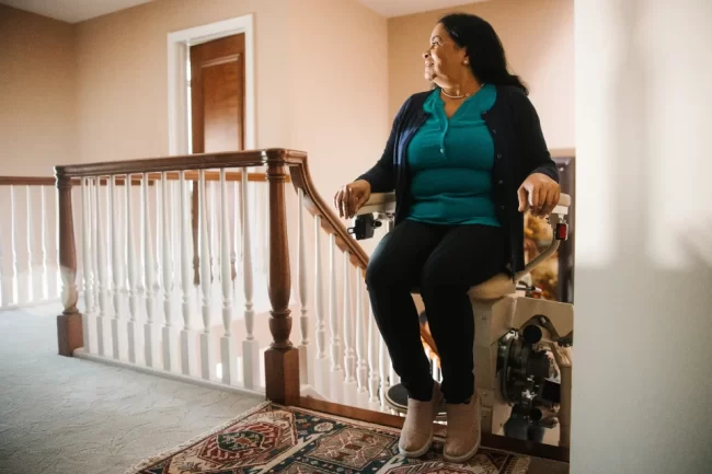 A woman prepares to step off of the stairlift she's sitting in.
