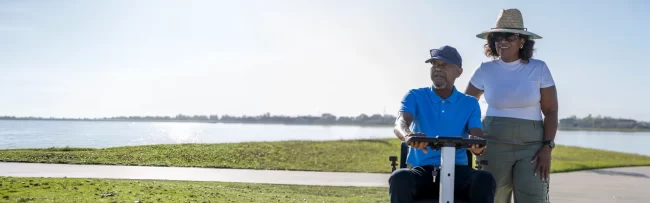 A man sitting on a mobility scooter with his wife standing nearby.