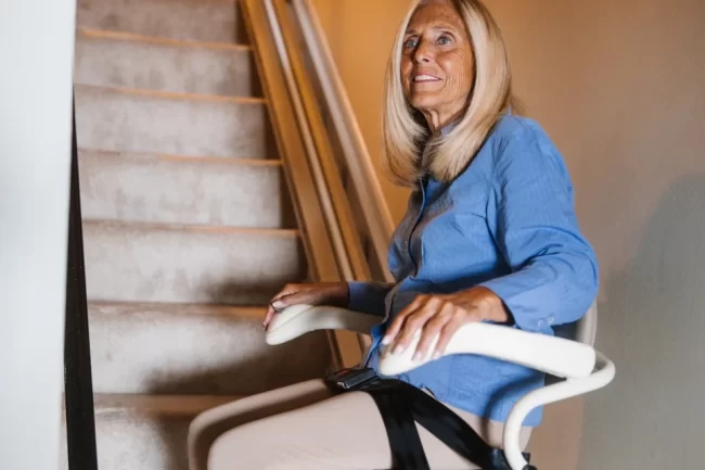 A woman strapped into a stairlift before ascending a staircase.