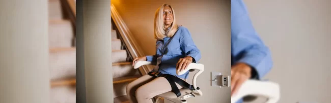 A woman sitting in her stairlift at the bottom of a staircase.