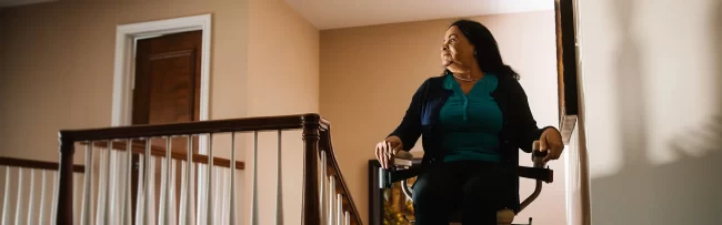 A woman sitting at the top of a staircase in her stairlift.