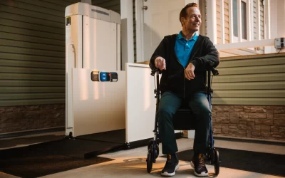A man sits near the vertical platform lift outside his home.