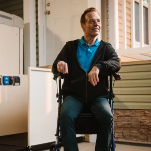 A man relaxes in a rolling walker in front of his vertical platform lift.