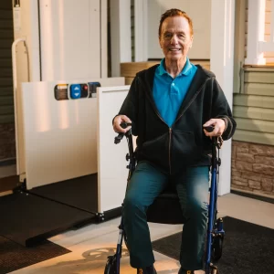 A man sitting in a rolling walker near a vertical platform lift at his home.